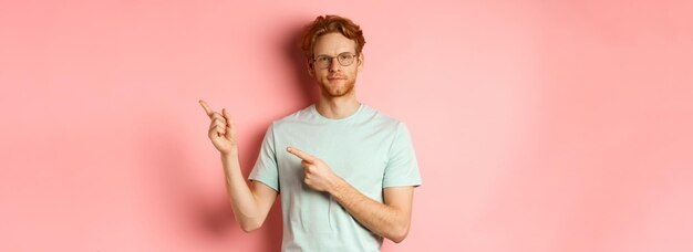 Selbstbewusster junger Mann mit roten Haaren und Bart lächelt zufrieden und zeigt mit dem Finger auf die Person oben rechts