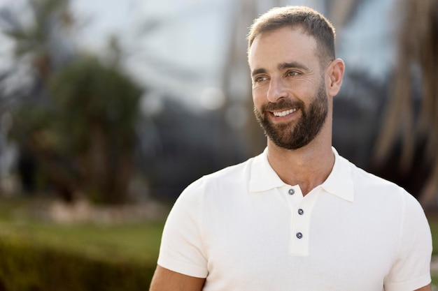 Selbstbewusster lächelnder hispanischer Mann mit weißem, stylischem T-Shirt, der auf der Straße wegschaut