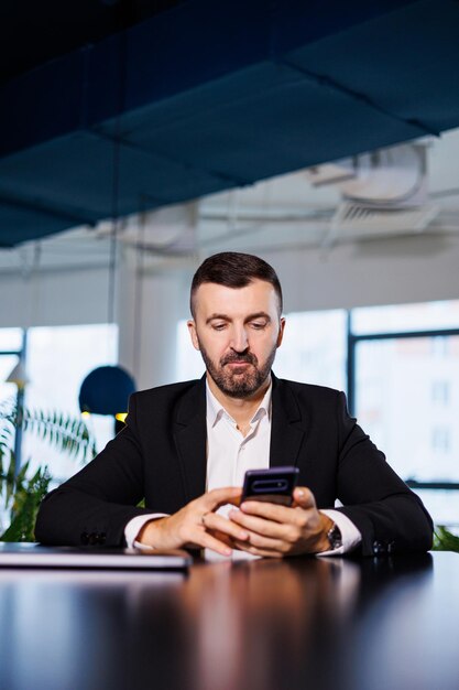 Selbstbewusster männlicher Geschäftsmann in einem Business-Anzug sitzt an einem Tisch mit einem Telefon und arbeitet aus der Ferne