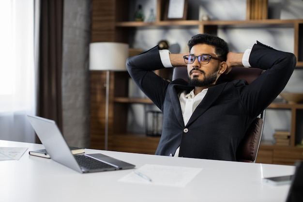 Selbstbewusster Mann mit Brille, der sich am Arbeitsplatz zu Hause entspannt, ein Nickerchen macht oder tagträumt