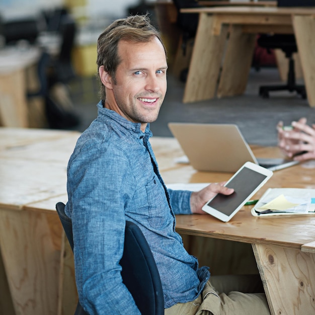 Foto selbstbewusster marketingmanager, der auf einem digitalen tablet in einem büro im internet surft gutaussehender und glücklicher profi, der kreative ideen recherchiert, um ein startup in sozialen medien zu fördern und zu bewerben