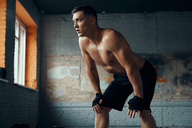 Foto selbstbewusster, muskulöser mann hält die hände auf dem knie, während er sich nach dem training im fitnessstudio ausruht