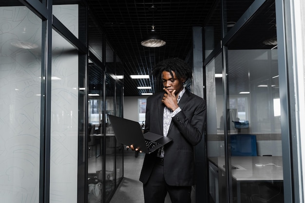 Selbstbewusster schwarzer Geschäftsmann mit Laptop, der online mit seinen Kollegen arbeitet. Schöner afrikanischer Manager im Büro.