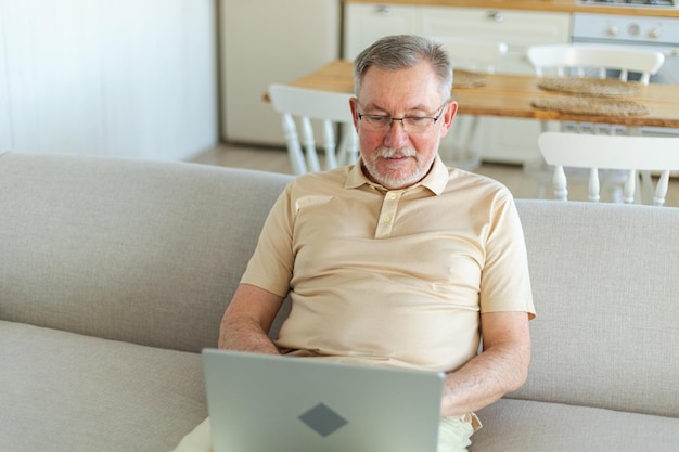 Selbstbewusster, stilvoller, glücklicher älterer Mann mittleren Alters, der zu Hause einen Laptop benutzt. Stilvoller älterer reifer Mann mit Bart