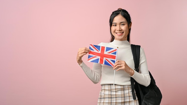Selbstbewusstes asiatisches Mädchen, das eine Flagge des Vereinigten Königreichs auf rosa isoliertem Hintergrund zeigt