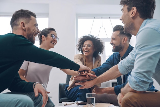 Selbstbewusstes junges Geschäftsteam, das sich die Hände hält und lächelt, während sie zusammen im Büro sitzen