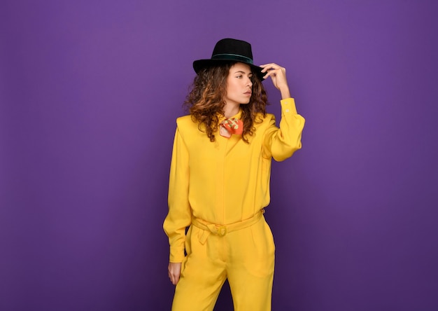 Selbstbewusstes junges stilvolles weibliches Modell mit langen lockigen Haaren in modischem leuchtend gelbem Retro-Anzug