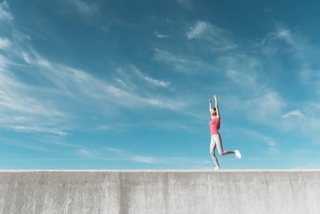 Selbstbewusstes schlankes Mädchen läuft unter blauem Himmel, treibt Sport und führt einen gesunden Lebensstil