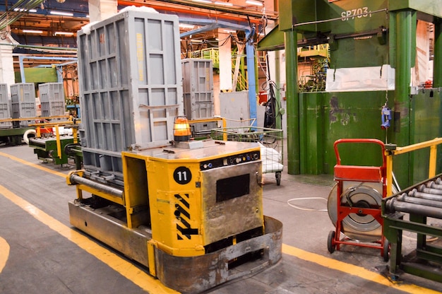Selbstfahrende autonome gelbe Metallkarrenmaschine mit Notlichtsignalisierung für den Warentransport in der Produktionshalle einer petrochemischen Ölraffinerie