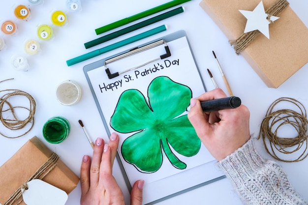 Selbstgemachte gemalte Grußkarte St. Patricks Day. Geschenkidee, Dekoration. DIY. Mach es selbst. Klee, Pinsel und Farbe. Weibliche Hände. St. Patricks Day-Hut.