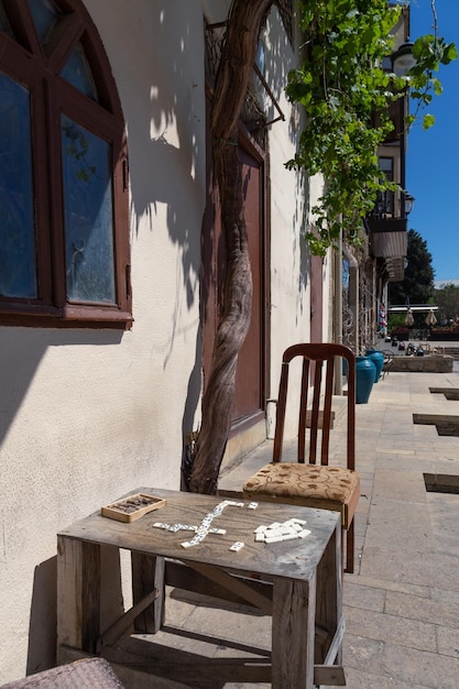 Selbstgemachter Holztisch mit Dominosteinen und abgenutztem Stuhl unter Baum im Haus in der Altstadt von Baku Aserbaidschan