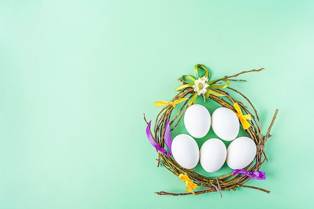 Selbstgemachtes Handwerksnest von Zweigen und bunten Bändern mit weißen Eiern auf grünem Hintergrund. Ostern Tischdekoration. Osterfestkomposition mit Kopierraum für Text.