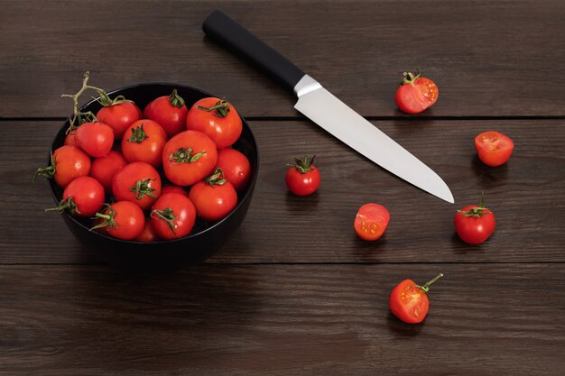 Selbstgezogene Kirschtomaten in einer schwarzen Schüssel auf einem dunklen Holztisch mit einem scharfen Messer daneben