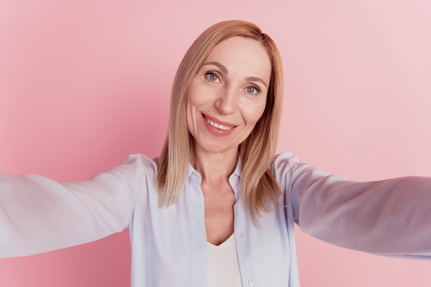 Selbstporträt einer hübschen jungen Frau in lässigem Outfit, die ein Selfie auf der Frontkamera auf rosafarbenem Hintergrund schießt