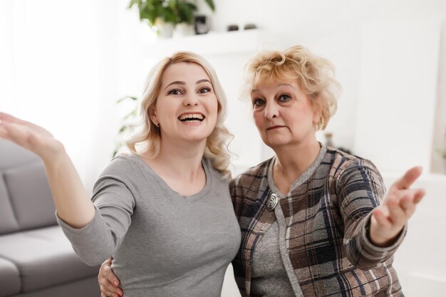 Selbstporträt einer ziemlich charmanten, positiven, funky Mutter und Tochter, die Selfie auf der Frontkamera mit Videoanrufen im modernen weißen Wohnzimmer schießen und die Freizeit genießen