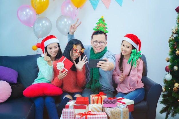 Selbstporträt von Mischrassefreunden: asiatische junge lächelnde bärtige Männer und Schönheiten im roten Weihnachtshut, der Konzept des neuen Jahres und der Feiertage aufwirft, feiert