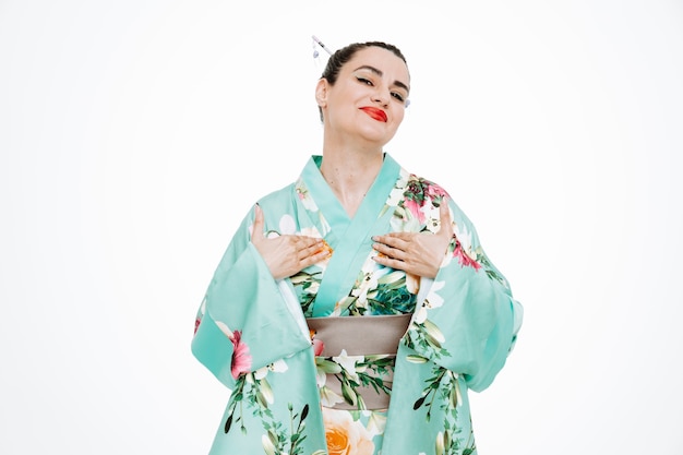 Selbstzufriedene Frau im traditionellen japanischen Kimono lächelt selbstbewusst und zeigt auf sich selbst auf Weiß