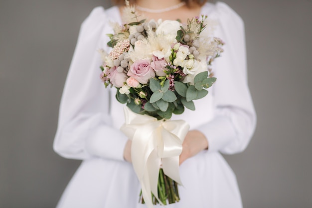 Foto seleção intermediária de noiva segura buquê de casamento nas mãos fundo cinza sessão fotográfica