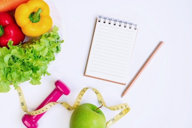 Selección de alimentación limpia de alimentos saludables con frutas, verduras, pesa, cuaderno y cinta métrica en blanco