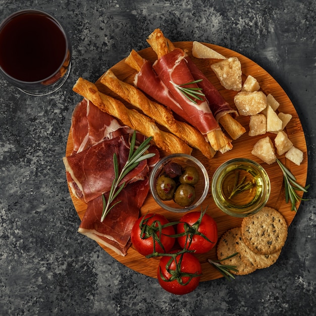 Selección de aperitivos de queso y carne. Jamón, parmesano, palitos de pan, aceitunas, tomates en tabla de madera.