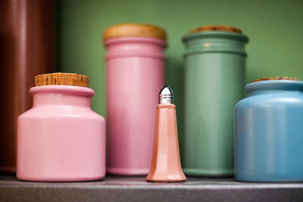 Selección de coloridos recipientes de cocina de cerámica o alfarería artesanal en un estante con enfoque selectivo a un salero rosa en primer plano en primer plano