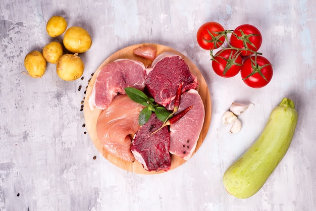 Selección de diferentes carnes crudas con verduras en el tablero de madera.