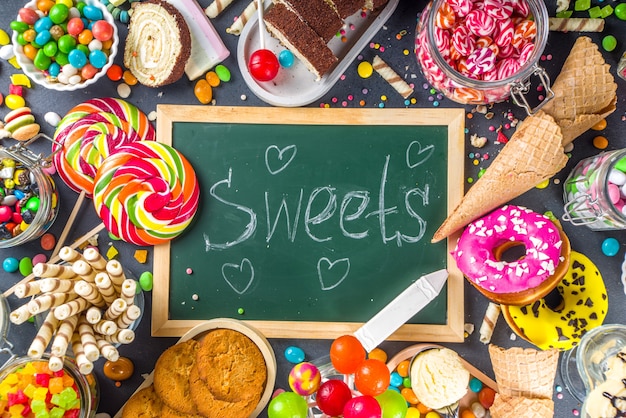 Foto selección de dulces coloridos. conjunto de varios caramelos, chocolates, donas, galletas, paletas, vista superior de helado sobre fondo de hormigón negro