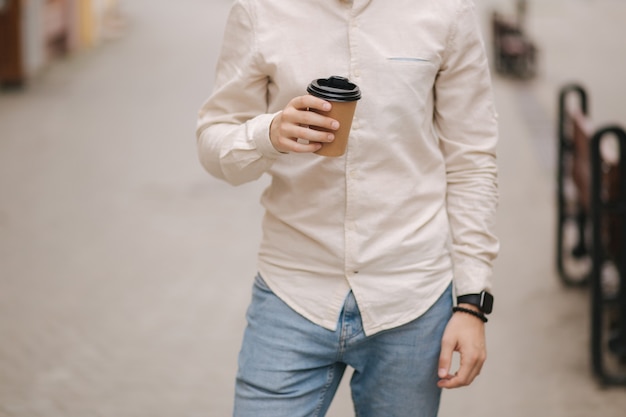 Selección intermedia de stand de hombre en la ciudad con taza de café.