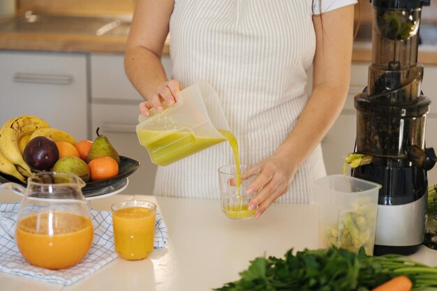 Selección media de una mujer vertiendo jugo fresco en un vaso de bebida verde vegetariana casera