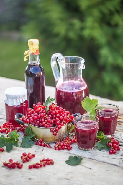 Una selección de productos de grosella roja - mosto de sirope de mermelada y vid roja en la mesa en el jardín.