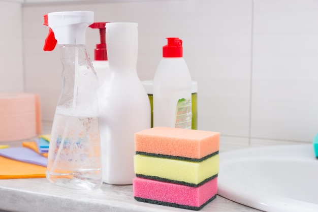 Selección de productos de limpieza domésticos en un baño con tres coloridos estropajos de esponja rociadores y paños