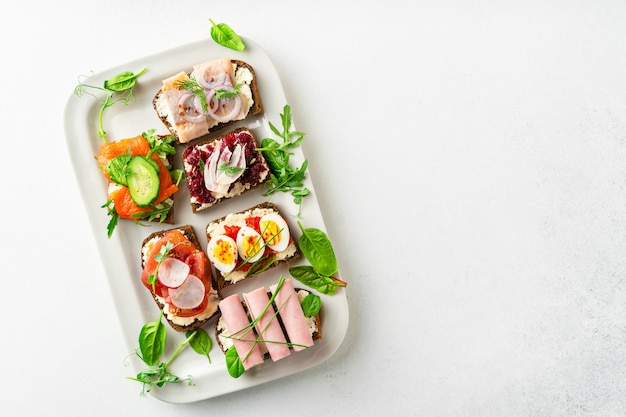 Selección de sándwiches abiertos smorrebrod daneses en un plato sobre la mesa blanca