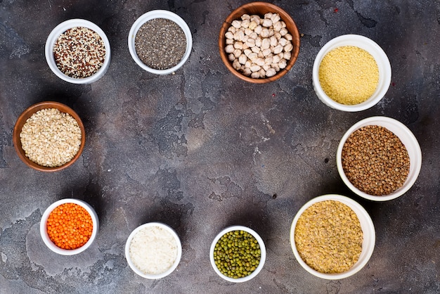 Selección de superalimentos y cereales en cuencos sobre fondo de hormigón gris.