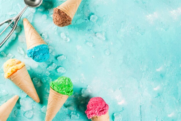 Foto selección de varios helados multicolores brillantes en conos de helado chocolate vainilla arándano fresa pistacho naranja sobre fondo azul claro soleado vista superior