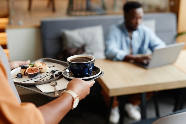 Selektive Fokusaufnahme einer nicht wiederzuerkennenden Frau, die im Café arbeitet und jungen Männern Kaffee und Dessert bringt.