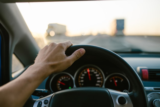 Selektive Fokusmannhand am Lenkrad, Autofahren bei Sonnenuntergang. Reise-Hintergrund.