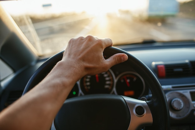 Selektive fokusmannhand am lenkrad, autofahren bei sonnenuntergang. reise-hintergrund.