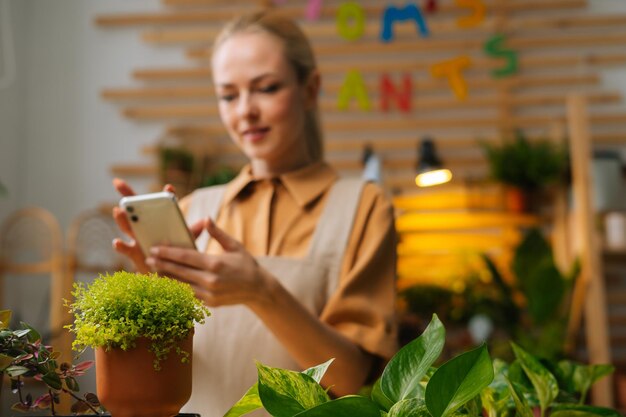 Selektive Fokussierung der bluurigen Floristin, die eine Nachricht an den Kunden tippt und mit dem Kunden auf dem Handy chattet und auf den Smartphone-Bildschirm schaut