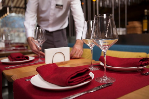 Selektiver Fokus auf ein Weinglas und einen Teller auf dem Tisch im Restaurant, Kellner, der am Hintergrund arbeitet