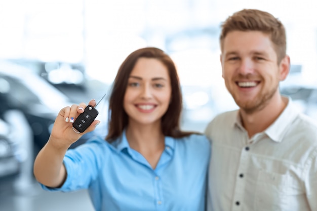 Foto selektiver fokus auf einen autoschlüssel schöne glückliche frau hält umarmung mit ihrem gutaussehenden ehemann in einem autosalon