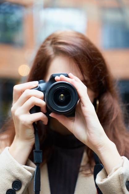 Selektiver Fokus auf Linse. Schönes stilvolles modernes Mädchen hält Kamera in ihren Händen und macht Fotos.