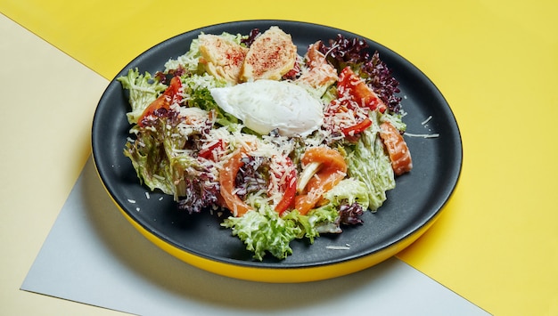 Selektiver Fokus auf servierten Caesar-Salat mit Lachs in schwarzer Platte. Leckerer Meeresfrüchtesalat