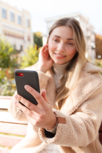 Selektiver Fokus auf Smartphone in der Hand einer schönen glücklichen Frau im Freien an einem sonnigen Herbsttag