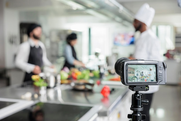 Selektiver Fokus der Kamera, die Küchenchefs des Restaurants filmt, die Gourmet-Gerichte für den kulinarischen Schulkurs zubereiten. Arbeiter der Lebensmittelindustrie drehen Kochvideos für Fernsehsendungen und Internet-Vlogs.