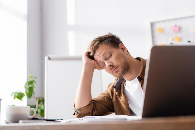 Selektiver Fokus eines erschöpften Geschäftsmannes, der auf einen Laptop auf einem Bürotisch blickt