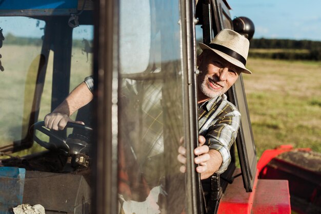 Foto selektiver fokus eines fröhlichen älteren landwirts, der einen traktor fährt