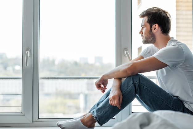 Selektiver Fokus eines gutaussehenden Mannes, der zu Hause auf der Fensterbank sitzt