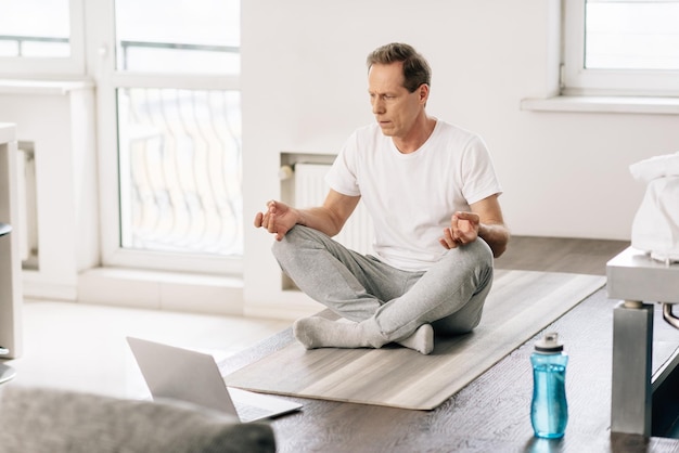 Selektiver Fokus eines Mannes in Socken, der in Lotus-Pose sitzt, während er sich Online-Übungen auf dem Laptop ansieht