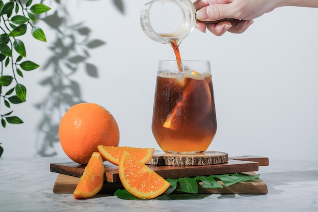 Selektiver Fokus kalt Iced Glas Espresso mit Orangensaft und frisch geschnittener Orange auf Holzplatte in weißem Hintergrund Sommercocktail Kalt gebrühter Kaffee oder schwarzer Tee Gießen kaltes Getränk