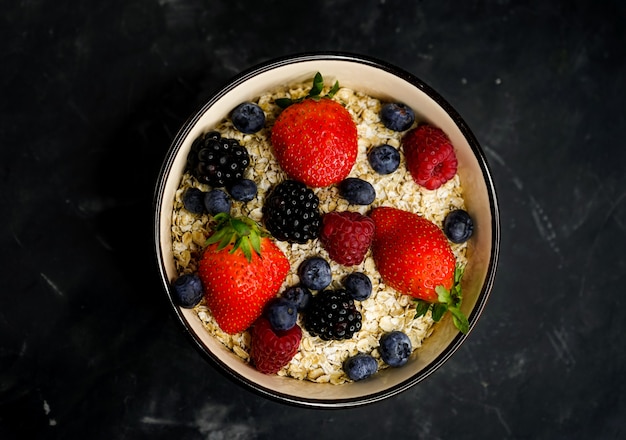 Selektiver Fokus, richtige Ernährung, gesundes Frühstück, tiefe Platte mit Müsli, Haferflocken, frischen Erdbeeren, Himbeeren, Blaubeeren und Brombeeren